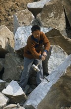 CHINA, Shaanxi Province, Xian, Man splitting rock in a stone quarry using a mallet and metal wedges