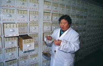 CHINA, Shaanxi Province, Xian, Woman weighing Chinese herbal medicines on hand held scales in front