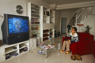 CHINA, Beijing, Modern domestic interior with young woman watching wide-screen television.
