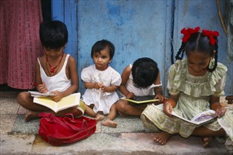INDIA, Maharashtra, Mumbai, Four children sitting cross-legged on the ground reading.