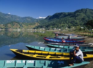 NEPAL, Annapurna Region, Pokhara, Painted wooden rowing boats on Lake Phewa with tree covered