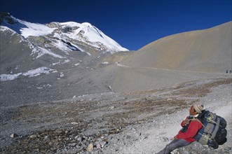 NEPAL, Annapurna , Porter carrying large back pack resting on the approach to Thorung La pass.