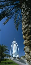 UAE, Dubai, The Jumeirah Beach Hotel with palm tree trunk in the foreground.