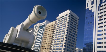 UAE, Abu Dhabi, Al-Ittihad Square.  Angled view of huge sculpture of a cannon with modern high rise