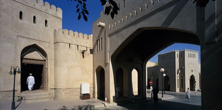 OMAN, Nizwa, Town centre with crenellated walls and archway over quiet street.  Man framed by