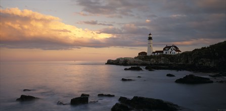 USA, Maine, Portland, Portland Head lighthouse on rocky headland with blue and gold cloudy sky