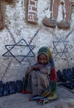 ETHIOPIA, Gonder Province, Felasher Village, Smiling young girl crouched beside typically decorated