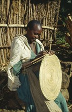 ETHIOPIA, Harerge Province, General, "Woman making circular mat from straw, stitched into place."
