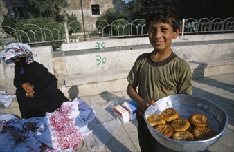 SYRIA, Central, Hama, "Young boy selling sweetmeats in the market, woman in traditional black dress