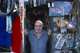 SYRIA, North, Halab, Male shopkeeper at the entrance to his shop with display of mixed goods