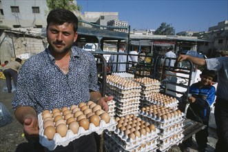 SYRIA, Central, Hama, "Man selling eggs in street market, standing holding tray with more stacked