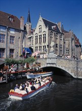 BELGIUM, West Flanders, Bruges, Tourists on canal boat trips below a bridge and old buildings