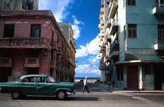 CUBA, Havana, An old green American car passing a side street that leads to The Malecon