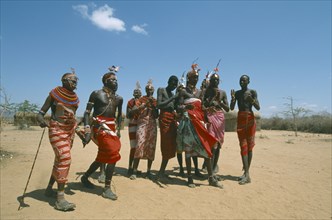 KENYA, Samburu, People, Samburu men and woman in traditional dress dancing in barren landscape.
