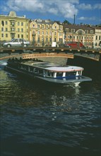 RUSSIA, St Petersburg, Moika Canal with tour boat passing underneath arched bridge with cars