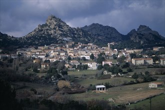 ITALY, Sardinia, Gallura, Aggius village. Houses built on a hillside with rock peaks behind.