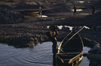 20017858 BANGLADESH  Jafflong Workers in stone quarry near water with man in foreground lifting basket of stones from wooden rowing boat.