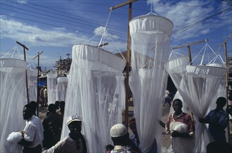 TANZANIA, Dar es Salaam, Mosquito nets for sale at market with men in the foreground and seen