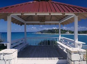 WEST INDIES, Antigua, Long Bay, Wooden decking with red painted roof and white seating framing view