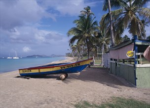WEST INDIES, Nevis, Pinneys Beach, Empty sandy beach fringed by palm trees with painted wooden boat