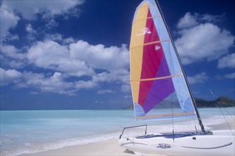 WEST INDIES, Antigua, Jolly Beach, Empty sandy beach with hobiecat with brightly coloured sail in