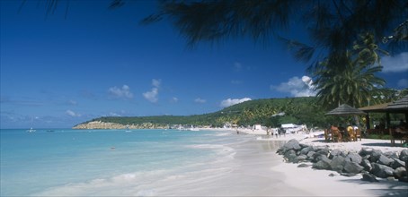 WEST INDIES, Antigua, Dickenson Bay, View along beach towards tree covered headland with people