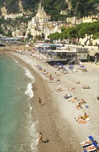 ITALY, Campania, Amalfi Coast, Amalfi.  View along shingle beach with sunbathers and cafes towards