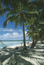 PACIFIC ISLANDS, Cook Islands, Aitutaki, Akitua.  Sandy beach with people sunbathing on wooden sun