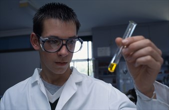 EDUCATION, Science Class, Male student wearing protective glasses and lab coat holding a test tube