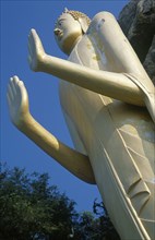 THAILAND, South, Hua Hin, Standing Buddha.  Angled view seen from below against blue sky.