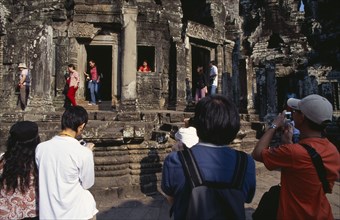 CAMBODIA, Siem Reap Province, Angkor Thom, The Bayon.  Tourists posing for photographs amongst the
