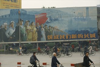 CHINA, Sichuan, Chengdu, ‘Building our new Great Wall’ poster on hoarding beside road with cyclists
