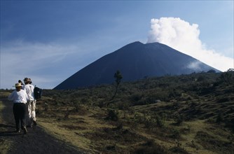 GUATEMALA, Pacaya Volcano, Smoking cone of volcano with people walking a dirt path in the