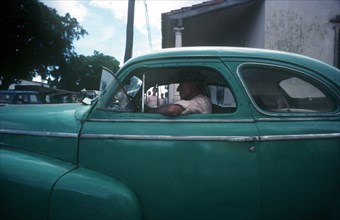 CUBA, Havana, Man driving a light green 1950 s car