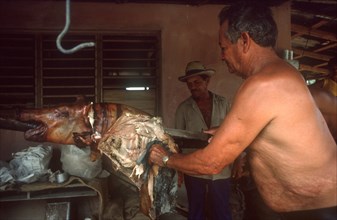 CUBA, Holguin, Palma Soriano, Man carving barbequed pig