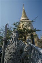 THAILAND, Bangkok, Grand Palace, Wat Phra Kaew. Statue standing by steps looking up to golden spire