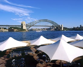 AUSTRALIA, New South Wales, Sydney, Harbour Bridge with restaurant umbrellas in the foreground