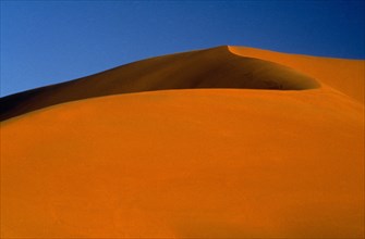 LIBYA, South West, Achan, Large orange desert sand dune with a clear blue sky