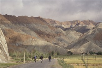 CHINA, Quinghai Province, Near Guide, Row of three cyclists on a road leading toward rocky mountain