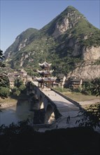 CHINA, Guizhou, Bridge over river with Temple built on the centre and mountain landscape behind
