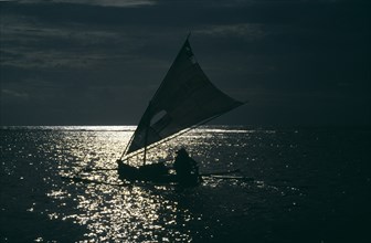 INDONESIA, Lombok, Gili Meno, Sailboat silhouetted in early evening sunlight reflected on the water