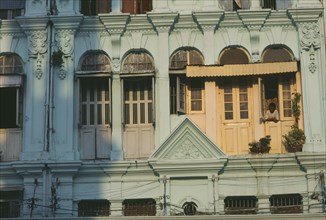 MYANMAR, Yangon, Detail of building facade with shuttered windows and man looking out.