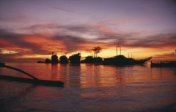 PHILIPPINES, Boracay Island, Rocky outcrops and moored boats silhouetted against pink and orange