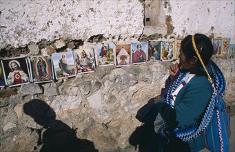 20026056 MEXICO Chiapas San Cristóbal de Las Casas Woman in front of coloured pictures of the lives of the Saints and Christ displayed along stone wall.