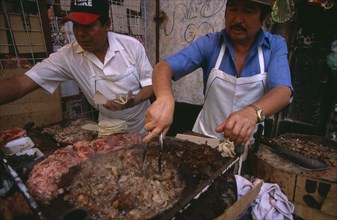 MEXICO, Mexico City, Men cooking meat for tacos and enchiladas on circular hot plate at roadside