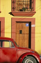 MEXICO, Oaxaca, Oxaca City, Partly seen red volkswagon beetle outside yellow building with wooden