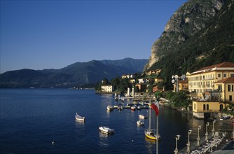 ITALY, Lombardy, Lake Como, Waterfront buildings overlooking moored boats with mountain landscape