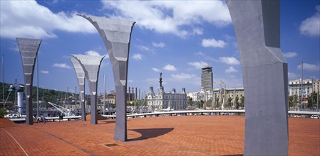 SPAIN, Catalonia, Barcelona, Port Vell.  Modern sculpture on paved area with masts of moored yachts