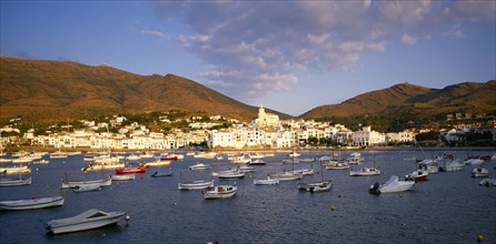SPAIN, Catalonia, Cadaques, View over moored boats towards white painted town at foot of steep