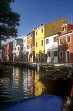 ITALY, Veneto, Venice, Burano Island.  Boats moored at canal-side overlooked by row  of brightly